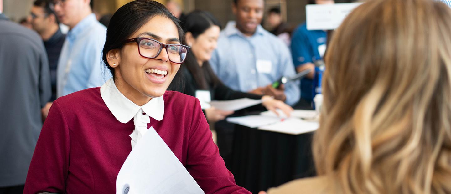 Young professionally dressed female student smiles as she talks to a corporate recruiter